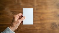 Mature man's hand holding blank white card against wooden background for mockup and branding purposes.