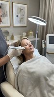 Professional cosmetologist performing facial treatment on relaxed middle-aged Caucasian woman in modern aesthetic clinic with specialized equipment.