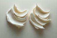 Soft peaks of white whipped cream or meringue swirled into decorative rosettes against neutral background, showcasing light and shadow detail in culinary photography.