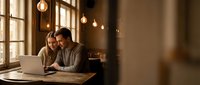 Young couple working together on laptop in cozy cafe with warm lighting and wooden interior for business collaboration and remote work.