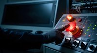 Professional operator activating emergency systems at industrial control panel with glowing red warning lights and monitoring equipment in dark facility.