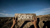 Hands holding wooden sign with sorry message against blue sky and rocky landscape for apology and forgiveness concepts in outdoor natural setting.