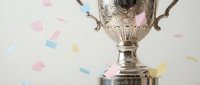 Ornate silver trophy cup with decorative handles and engraved details surrounded by colorful confetti pieces on white background for celebration concepts.