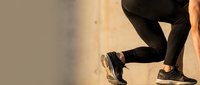 Runner in black leggings and sneakers jogging against neutral background, ideal for fitness, sports, and wellness marketing materials.
