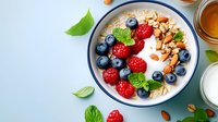 Creamy yogurt bowl with fresh blueberries, raspberries, crunchy almonds and mint leaves arranged on light blue background. Healthy breakfast concept.
