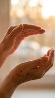 Elderly hands in protective gesture with warm sunlight, symbolizing care, safety, security and guardianship for healthcare and insurance concepts.