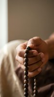 Hands holding wooden prayer beads in meditation pose with soft natural lighting for spiritual wellness and mindfulness practices.