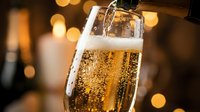 Champagne being poured into a glass with golden bokeh lights in the background, suitable for celebration and festive event photography.