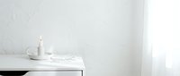 Minimalist white desk workspace with candle, scattered papers, and natural light from window for modern office design projects.