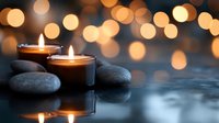 Glowing candles and zen stones on reflective surface with warm bokeh lights in background creating peaceful spa atmosphere for wellness and relaxation.