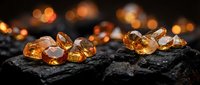 Golden amber gemstones scattered on dark volcanic rock surface with warm bokeh lights creating luxurious jewelry and mineral collection atmosphere.