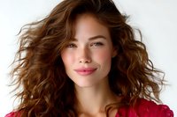 Young Asian woman with wavy brown hair wearing red sweater smiling at camera against white background, natural makeup and fresh glowing skin for beauty and fashion content.