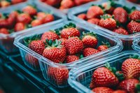 Fresh ripe strawberries in transparent plastic containers at farmers market, showcasing vibrant red color and natural green stems.