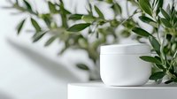 White cosmetic cream jar on marble surface with fresh green olive leaves and soft shadows, minimalist skincare product photography for beauty and wellness.