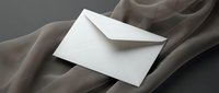 White envelope on flowing beige silk fabric creates elegant minimalist composition for luxury correspondence and wedding stationery designs.