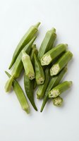 Fresh green okra pods whole and sliced showing seeds on white background isolated for cooking and healthy eating concepts.
