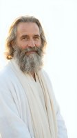 Mature Caucasian man with long gray hair and full beard wearing white robes smiling peacefully outdoors in soft natural light for spiritual wellness content.