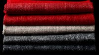 Stack of colorful burlap fabric rolls in red, white, gray and black arranged horizontally showing natural jute textile material for crafting and decoration.