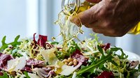 Male hand drizzling golden oil over fresh mixed green salad with vegetables, ideal for food, cooking, nutrition and restaurant marketing materials.