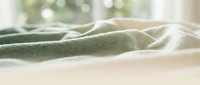 Soft sage green linen fabric draped on neutral surface with natural window light creating gentle shadows and highlights, suitable for textile and home decor projects.
