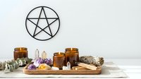 Pentagram symbol with amber glass bottles, crystals, sage bundle and candles arranged on wooden tray for spiritual wellness and alternative healing practices.