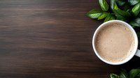 Hot chocolate or cocoa drink with frothy milk foam in white ceramic cup on dark wooden table with fresh green leaves, top view with copy space.