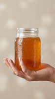 Cold iced tea or beverage in glass jar held by woman with manicured nails against neutral background. Refreshing drink for summer.