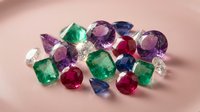 Collection of precious gemstones including emeralds, rubies, sapphires and amethysts scattered on pink surface for jewelry making and luxury accessories.