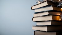 Stack of hardcover books against light background with dramatic side lighting creating shadows and depth. Minimalist composition for education and literature concepts.