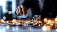 Professional in business suit examining architectural model of modern residential complex with glowing city lights and bokeh effect in background.
