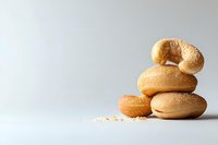 Fresh bagels stacked in minimalist composition on light background with sesame seeds scattered, showcasing artisanal bread variety and texture.