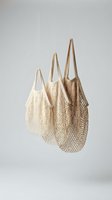 Three natural cotton mesh shopping bags hanging against neutral background showcasing sustainable zero waste lifestyle and eco-friendly grocery shopping.