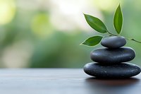 Balanced black spa stones pyramid with fresh green leaves on wooden surface against soft bokeh background, symbolizing harmony and wellness.