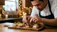 Professional male chef in apron carefully plating gourmet appetizers on wooden board in warm restaurant kitchen with festive lighting atmosphere.