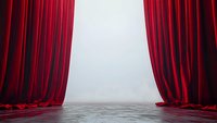 Luxurious red velvet curtains frame empty stage with concrete floor and bright spotlight creating dramatic theatrical atmosphere for performance space.