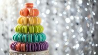 Colorful rainbow macarons stacked in pyramid tower against sparkling bokeh background for bakery, dessert menu, celebration and gourmet food concepts.