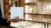 Woman holding blank white card in jewelry store with display cases in background, suitable for retail marketing, product promotion, and commercial advertising campaigns.