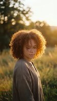 Young African American woman with curly afro hair in golden sunset light outdoors, natural beauty portrait with warm bokeh background for lifestyle content.