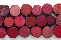 Collection of red and burgundy lipstick samples arranged in rows showing various shades and textures for cosmetic color palette and makeup artistry.