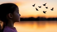 Young Asian girl in profile gazing at flying birds silhouetted against golden sunset sky over calm lake waters, creating peaceful dreamy atmosphere.