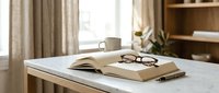 Cozy home office workspace with open book, reading glasses and coffee mug on wooden desk. Warm natural lighting creates peaceful study atmosphere for learning.