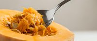 Fresh spaghetti squash being scraped with fork showing golden strands ready for healthy low-carb pasta alternative cooking preparation.