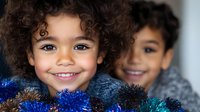 Cheerful young child with curly hair and bright smile holding colorful tinsel decorations during winter holiday season, expressing joy and festive spirit.