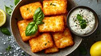 Crispy golden fried mozzarella sticks served with creamy ranch dipping sauce, fresh basil leaves and lemon wedges on dark plate. Appetizing party food.