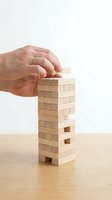 Hand placing a wooden block on a stacking tower game, symbolizing risk, strategy, balance, and business challenge concepts.