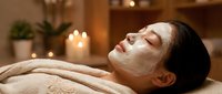 Young Asian woman relaxing with white facial mask treatment at luxury spa with candles and warm lighting for skincare and wellness routine.