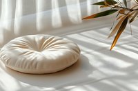Cream round floor cushion with tufted design on white fabric surface, casting soft shadows with dried botanical branch nearby for home decor and interior styling.