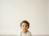 Young child with curly brown hair and mixed ethnicity, wearing a light beige t-shirt, smiling at camera against neutral background. Suitable for parenting, childcare, family lifestyle and educational content.