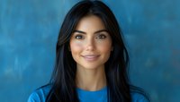 Young Hispanic woman with long dark hair smiling warmly at camera wearing blue top against textured blue background for professional headshot photography.