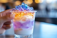 Colorful layered cocktail with purple and orange gradients topped with blue ice cubes in glass, close-up view against blurred background. Creative mixology.